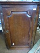 An antique oak corner cupboard having a panelled door with three scalloped edge shelves to the