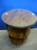 A circular teak and rosewood effect topped occasional table, glass topped with open shelves below,