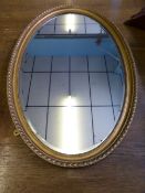 An oval hall mirror having bevelled glass in a decorative gilded frame with beaded decoration,