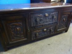 An Edwardian carved oak chest having a cupboard to each side with two drawers to the centre, the