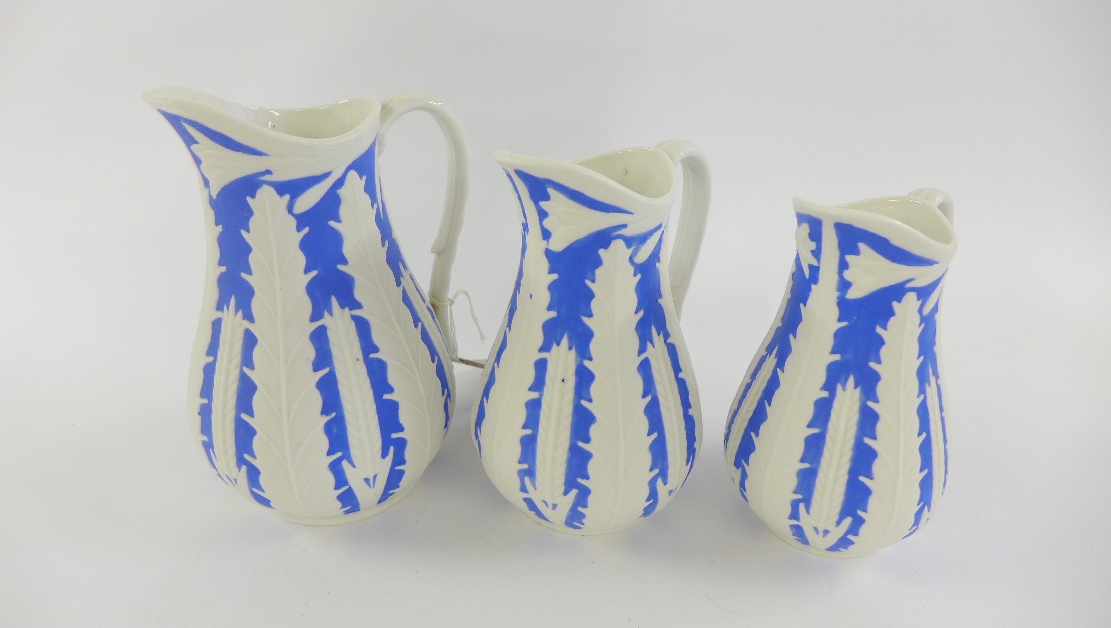 Three Staffordshire graduated wheat pattern relief moulded jugs in blue and white with Registration