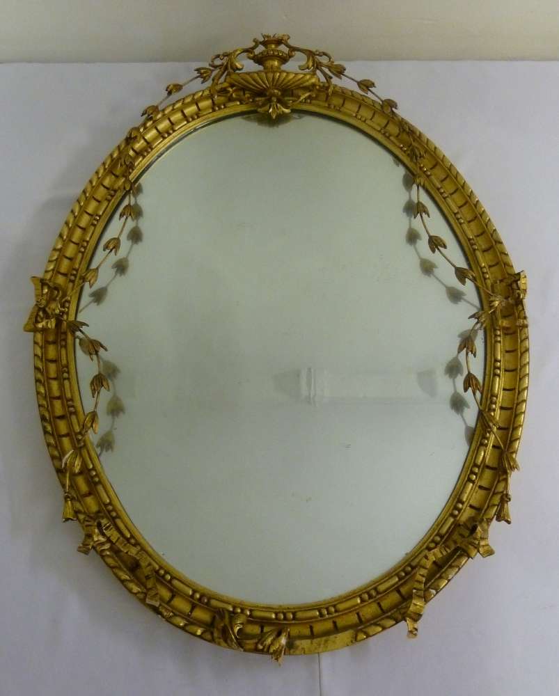 A classical style oval gilt mirror surmounted by an urn A/F