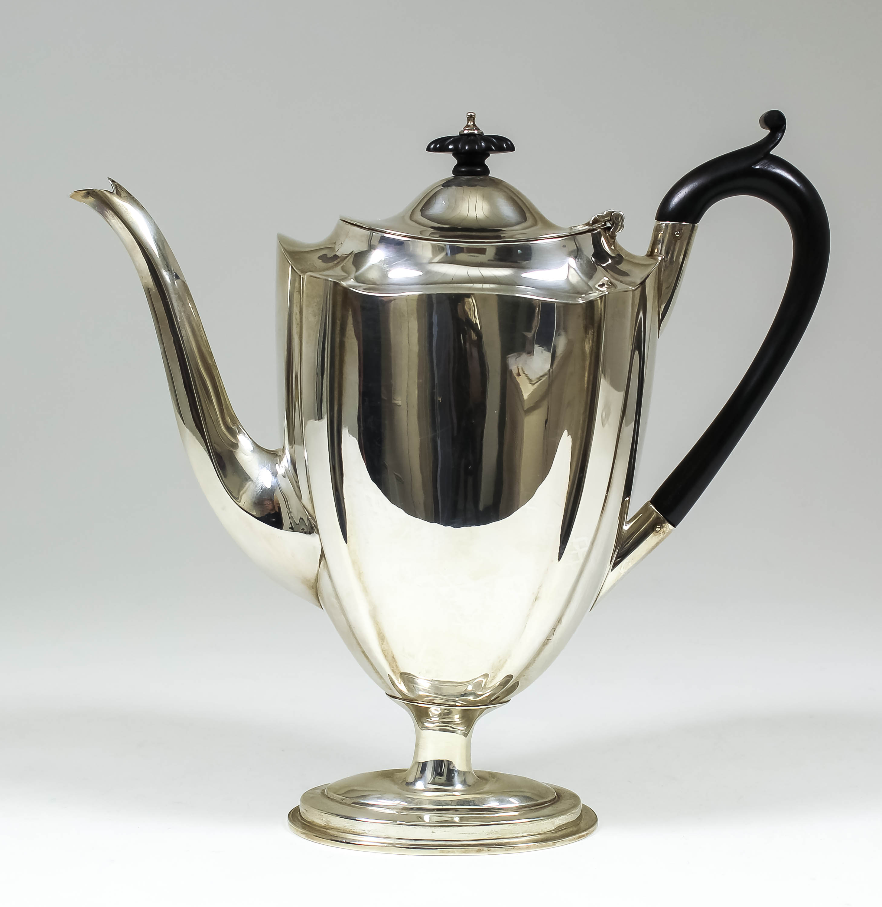 A late Victorian silver coffee pot of panelled form with ebonised scroll handle, on oval moulded