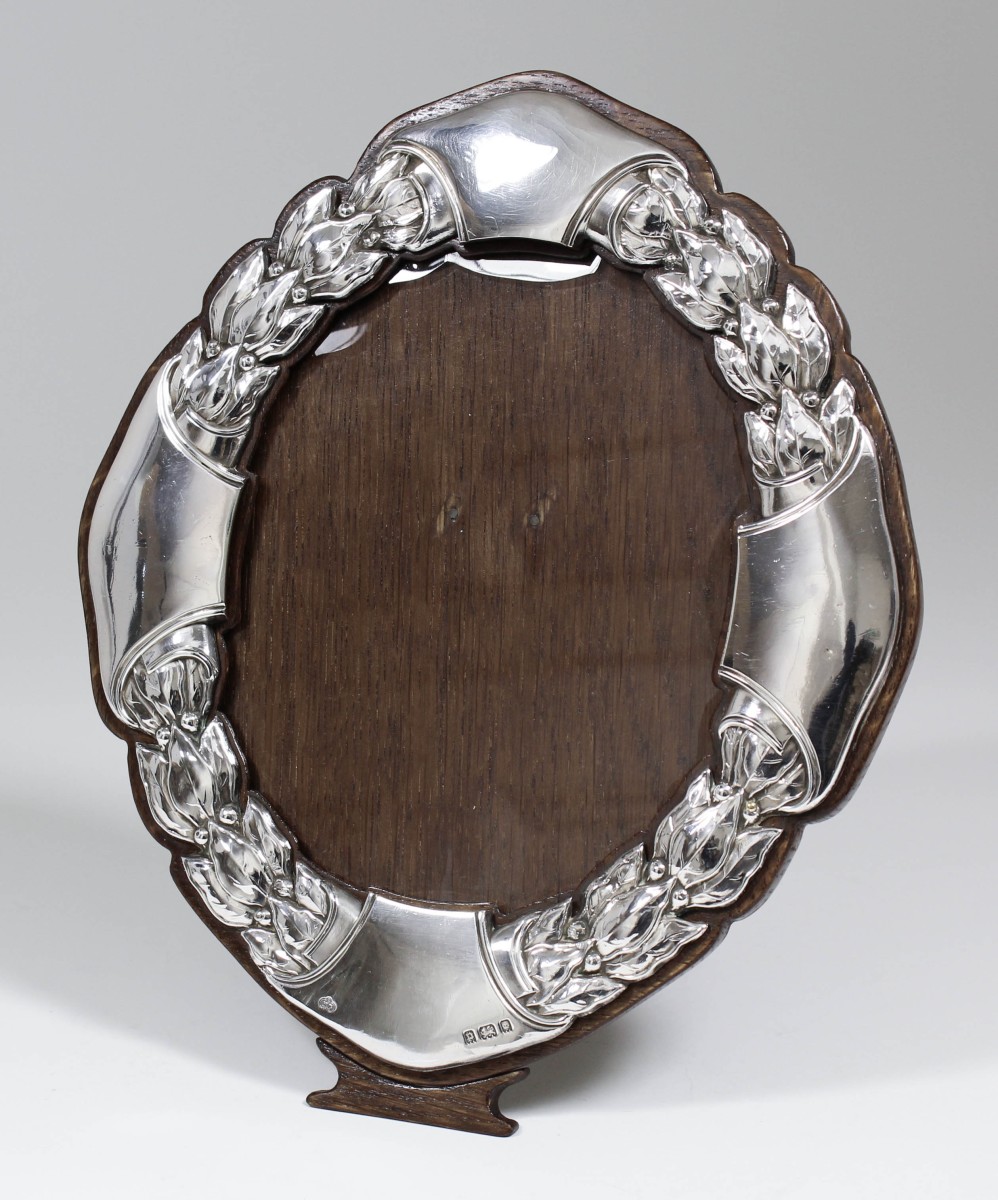 A George V silver oval photograph frame, the border embossed with bellflowers, 9.5ins x 7.75ins