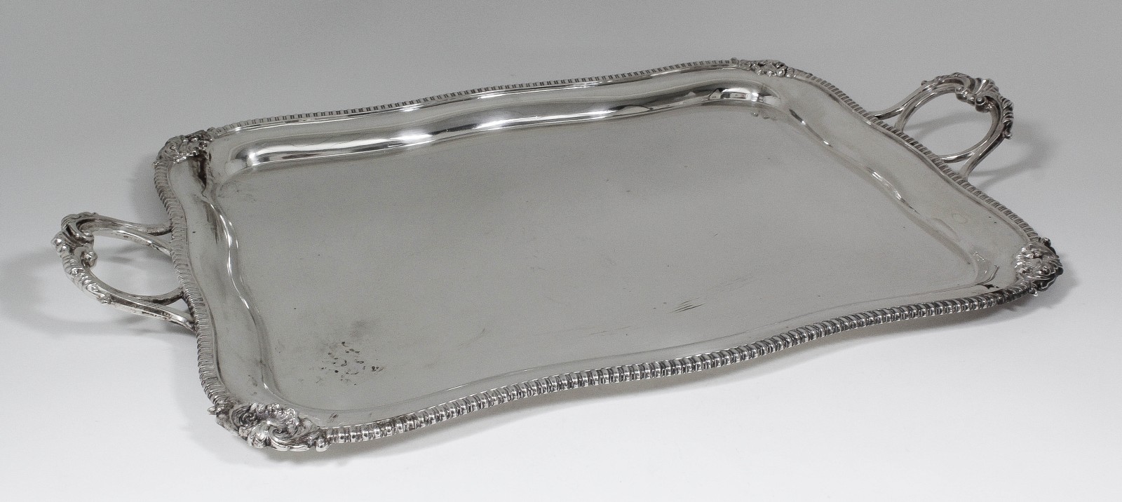 A George V silver rectangular two-handled tray with bold cast tongue pattern mounts to rim and with