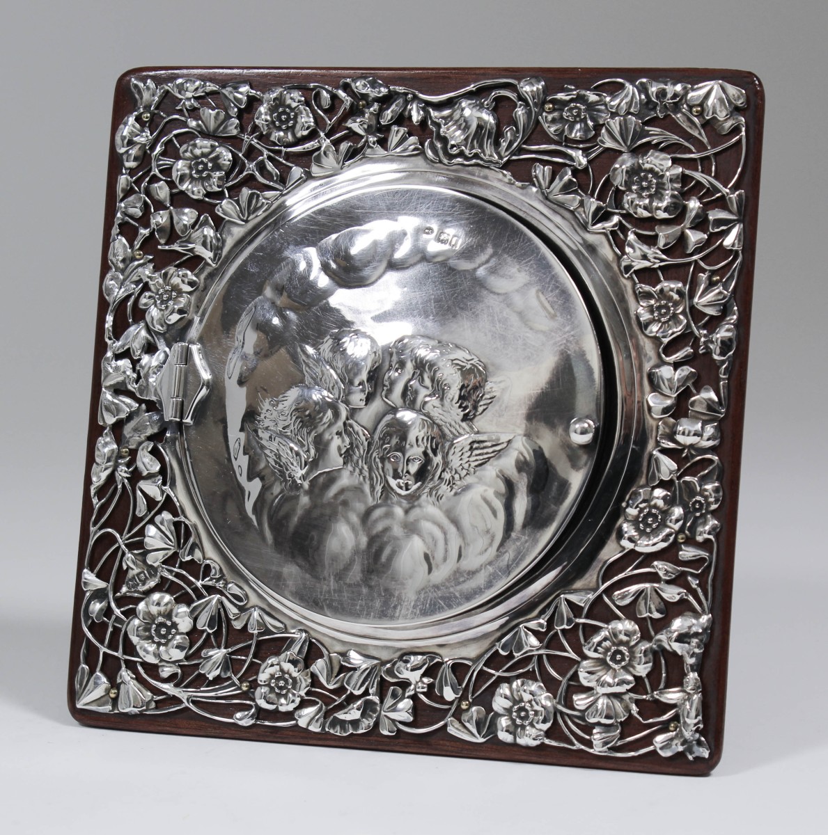 An Edward VII silver square photograph frame, the hinged circular cover embossed with cherubs heads