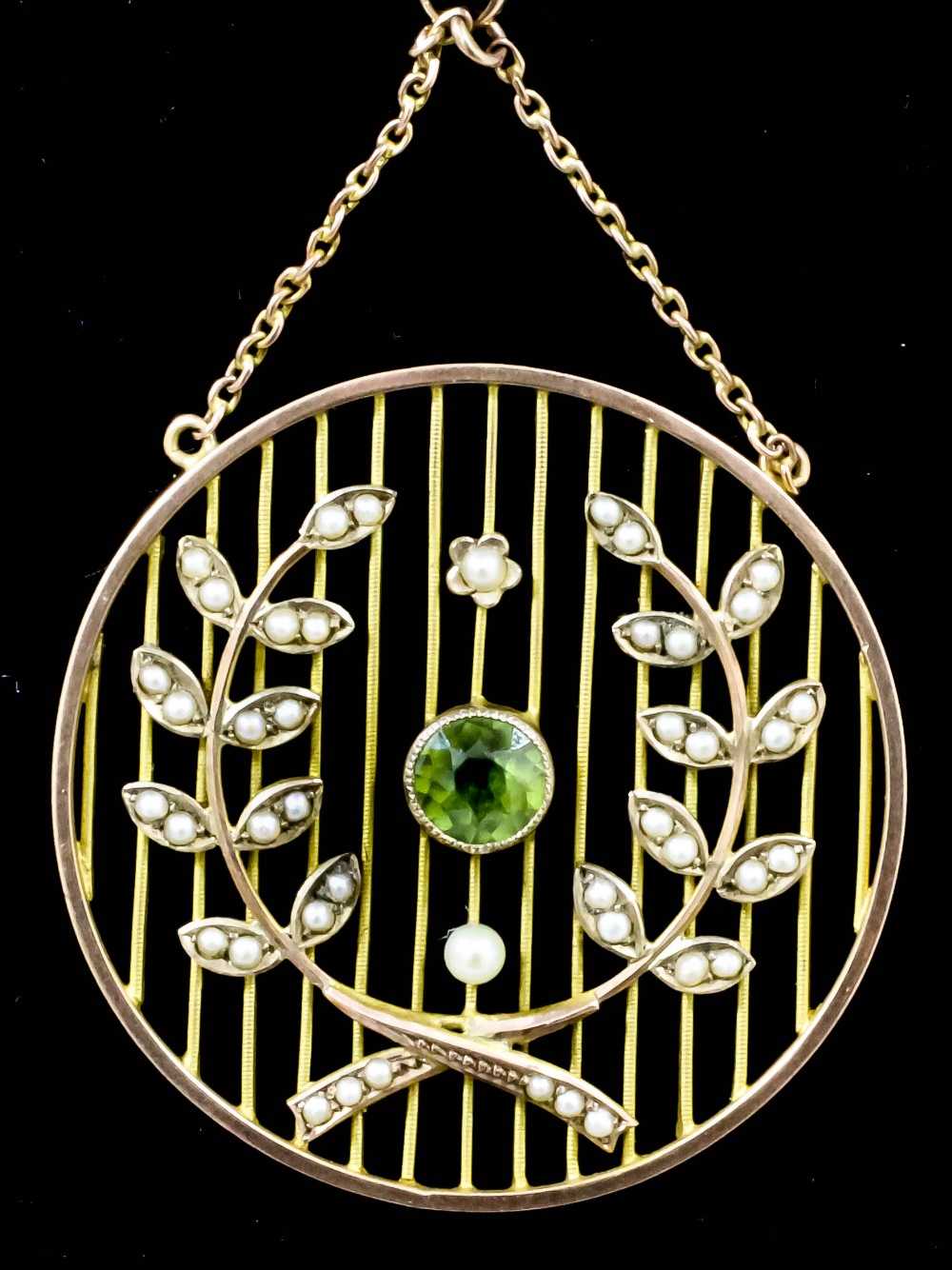 An Edwardian gold coloured metal peridot and seed pearl set circular pattern pendant, the open bar