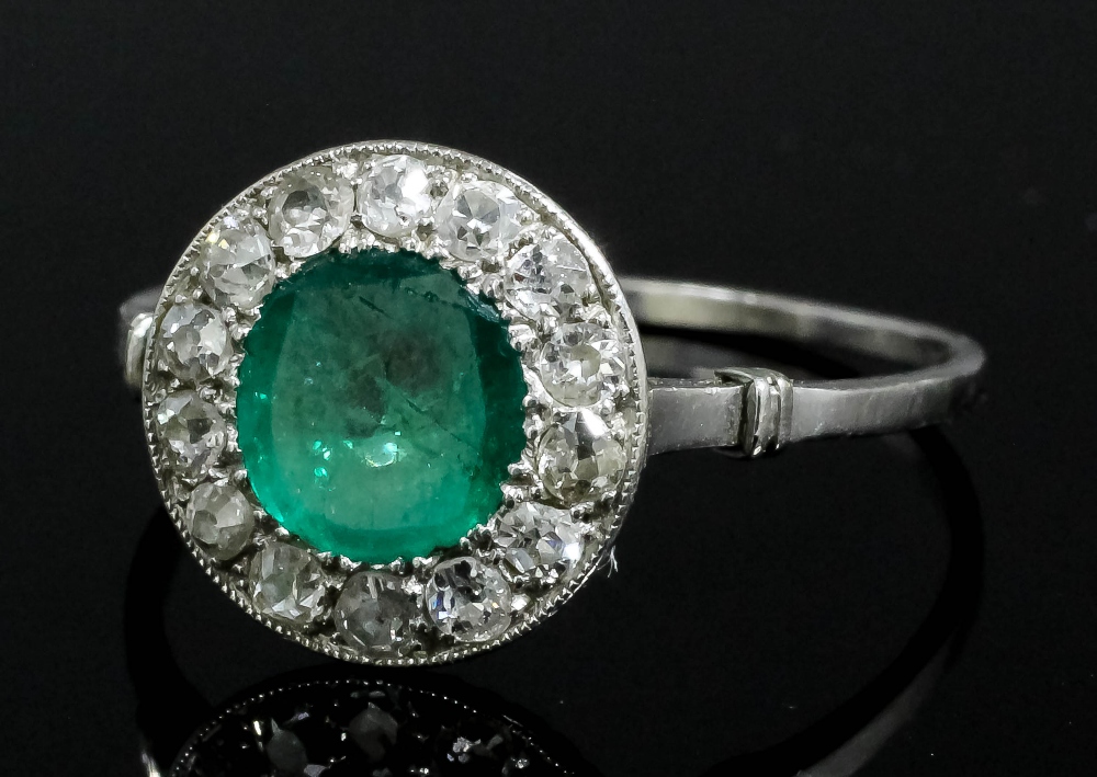 An Edwardian silvery coloured metal mounted emerald and diamond dress ring, the circular flat cut