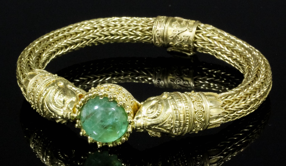 A gold coloured metal stiff bangle, set to  centre with a cabochon cut emerald (18mm diameter)