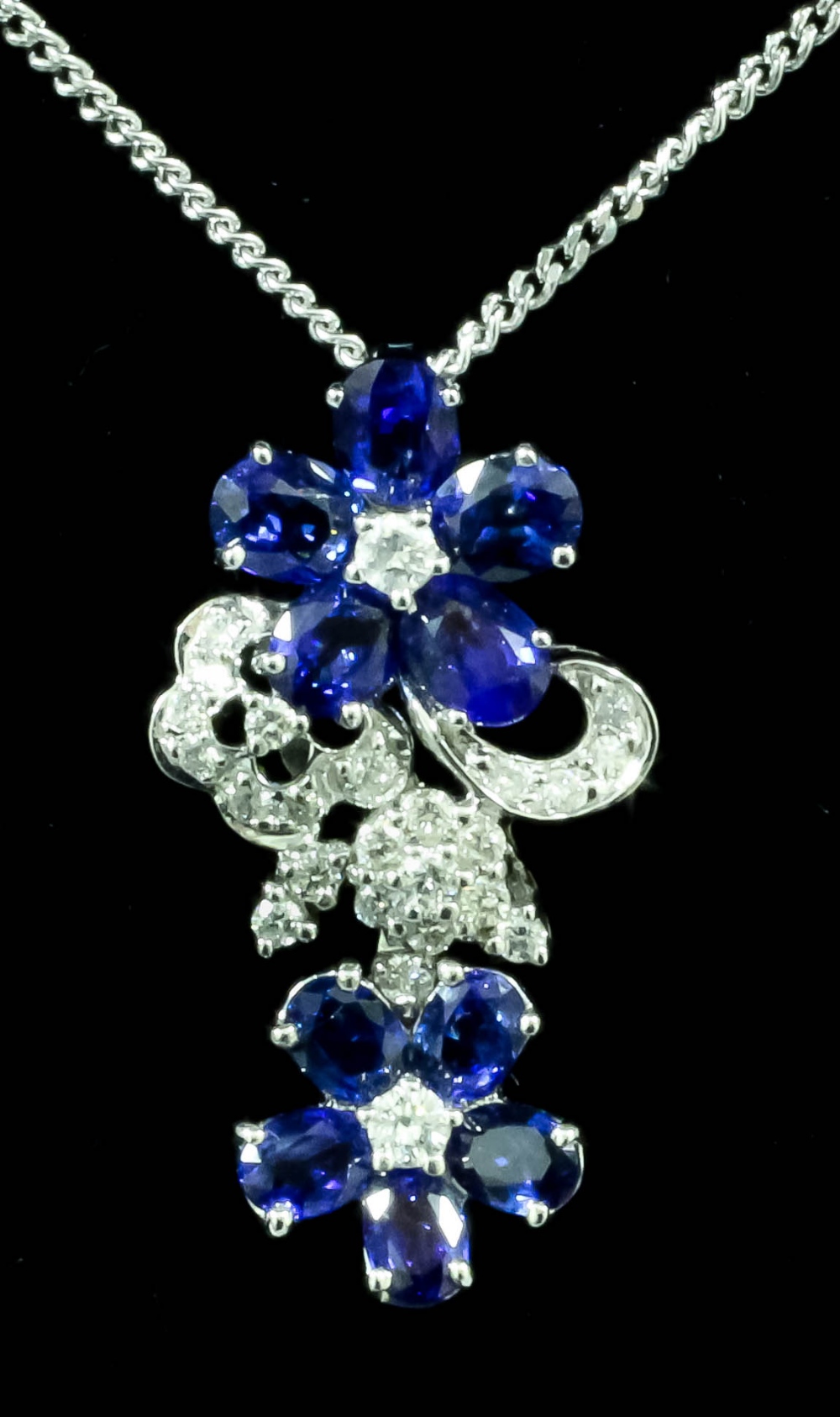 A modern 18ct white gold mounted gold and sapphire set flowerhead pattern pendant, the face set with