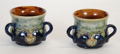 PAIR OF EARLY TWENTIETH CENTURY ROYAL DOULTON MOULDED POTTERY THREE HANDLED TYG PATTERN CUPS, of