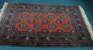 PAKISTAN SARIQ MAURI RUG, the red field decorated with rows of brown guls within a broad border of