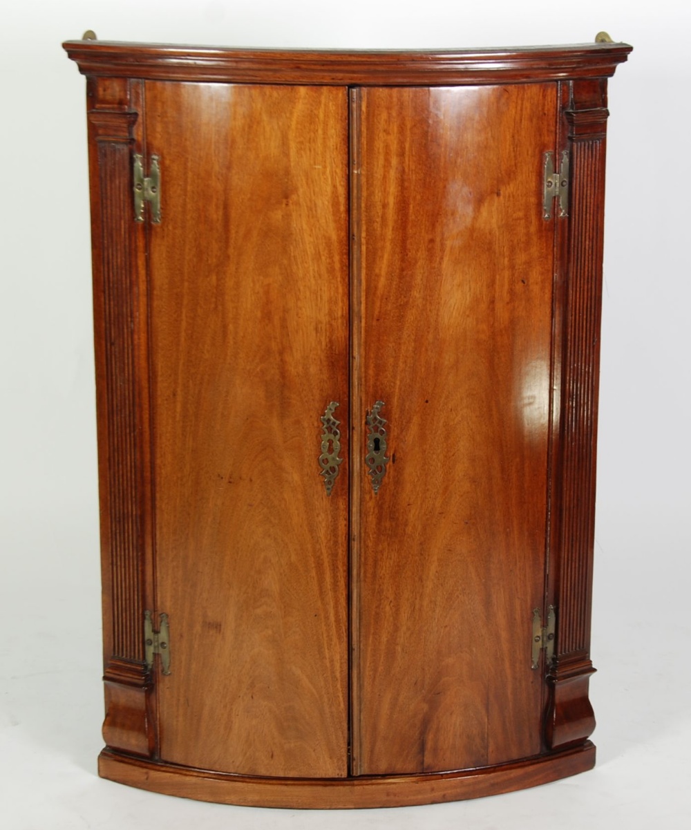 GEORGIAN MAHOGANY BOW FRONT CORNER CUPBOARD, the moulded cornice above a pair of cupboard doors