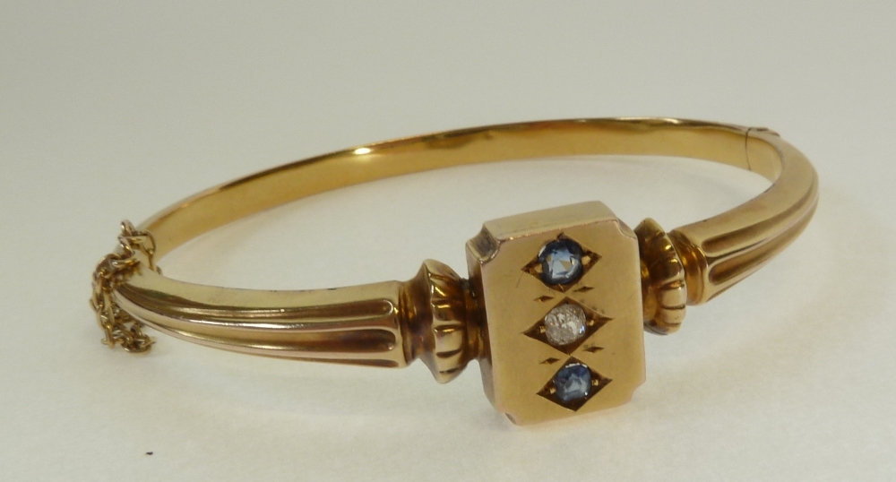 AN EARLY TWENTIETH CENTURY GOLD, DIAMOND AND SAPPHIRE SET HINGE OPENING BANGLE, the rectangular