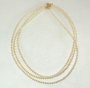A TRIPLE STRAND NECKLACE OF UNIFORM CULTURED BUTTON PEARLS, with plated clasp, in case