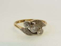 A STAMPED 18CT GOLD AND PLATINUM DIAMOND CROSS OVER RING, diagonally bezel set with three