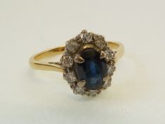 A STAMPED 18CT GOLD SAPPHIRE AND DIAMOND CLUSTER RING, claw set with an oval cut sapphire, with