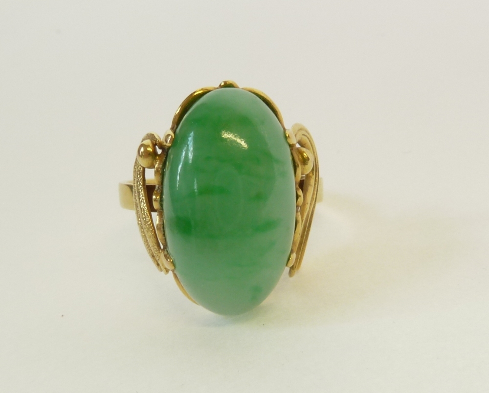 A STAMPED 14CT GOLD JADE CABOCHON SET RING, the oval claw set cabochon with brushed gold wing