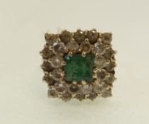 AN EMERALD AND DIAMOND CLUSTER RING, the cushion cut claw set emerald with a two tier surround of 28