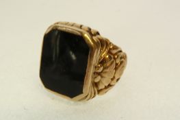 A GENT`S STAMPED 9CT GOLD SIGNET RING, with broad scroll shoulders and black stone inset top, 10.2g