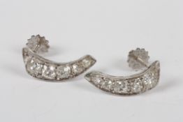 A pair of Art Deco style white metal and diamond earrings, of curved form and each set with five