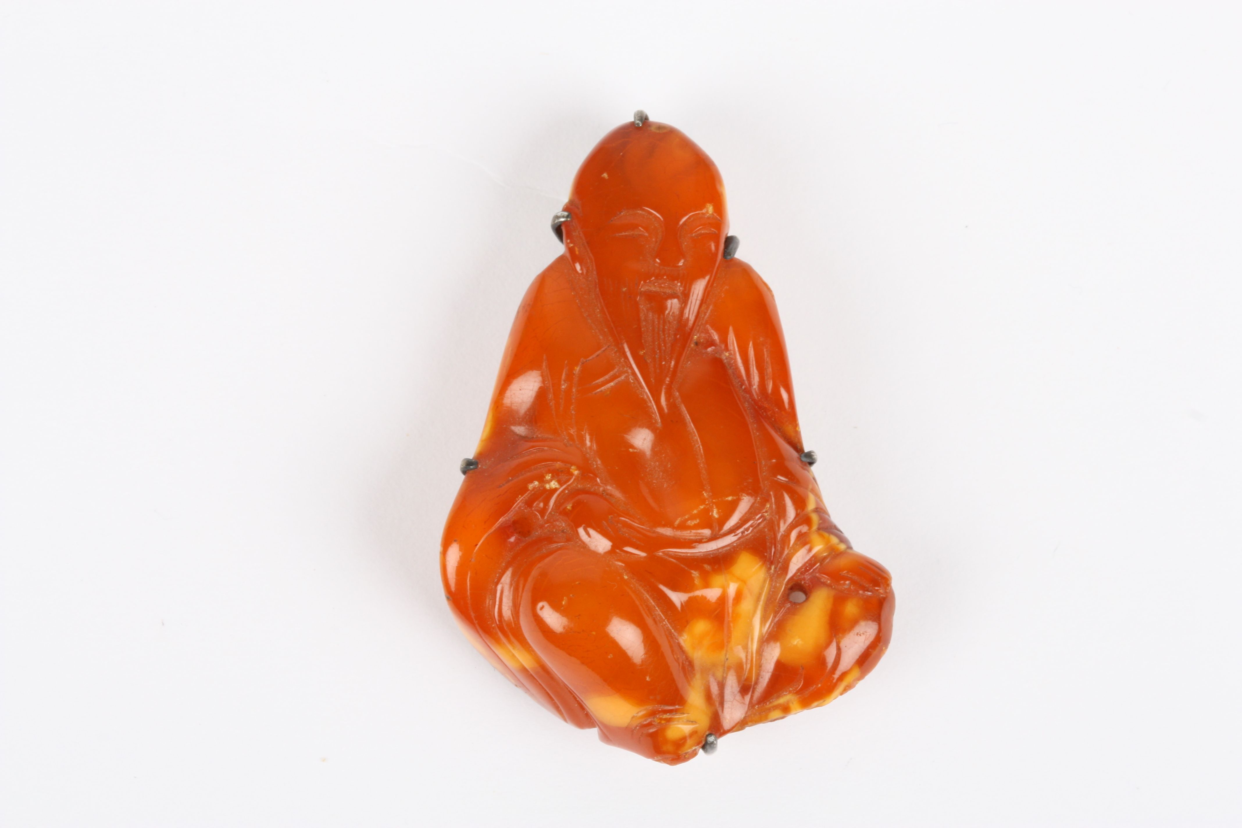 An early 20th century Chinese carved amber coloured pendant of a Buddha, in seated pose, and held