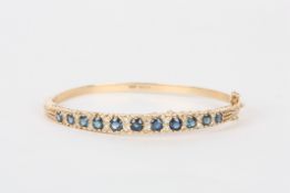 A 9ct gold Victorian style sapphire and diamond stiff bangle, set with eleven graduated sapphires