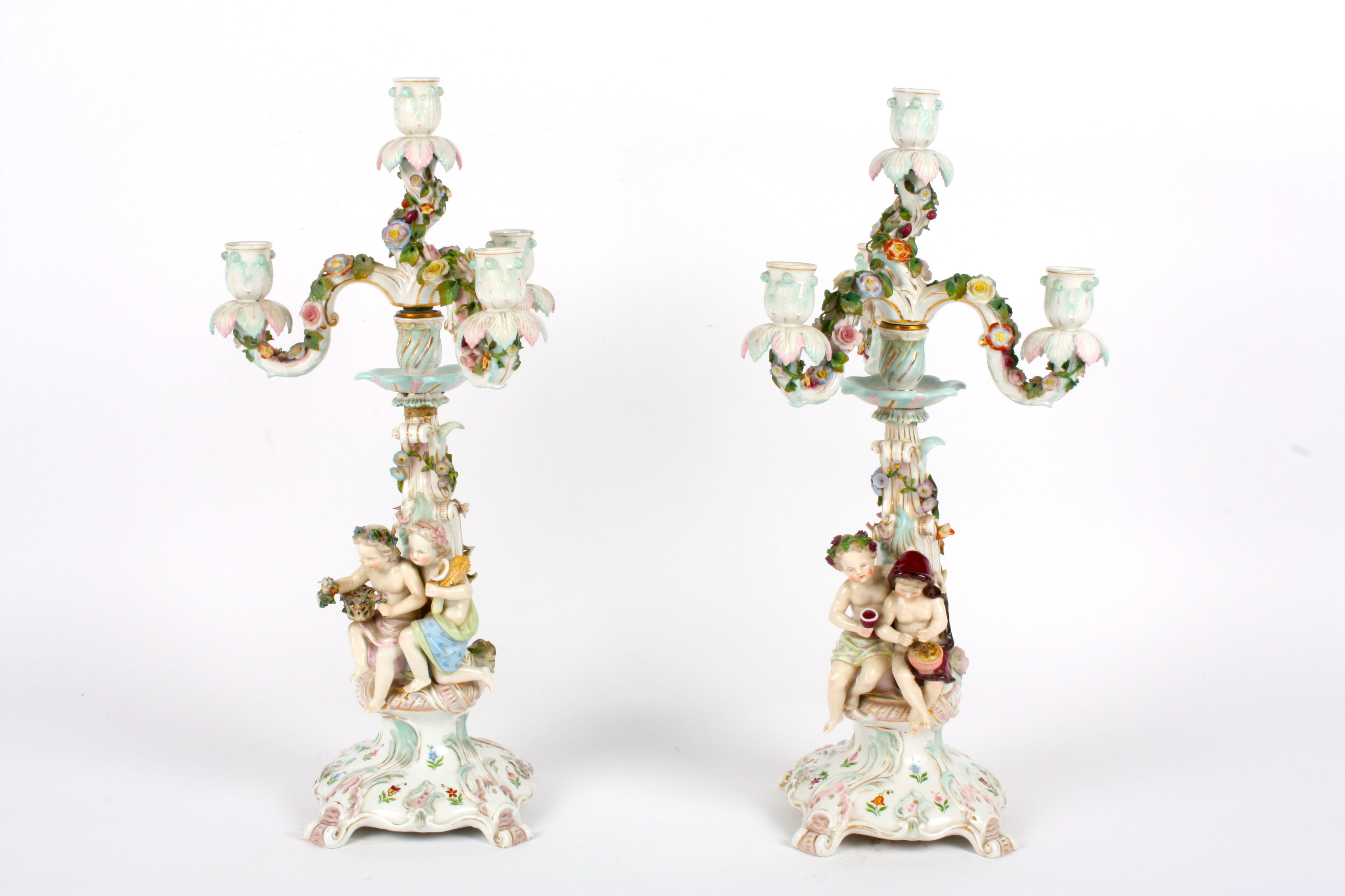 A pair of Continental figural candelabra, the scroll shaped central columns heavily decorated with