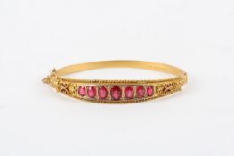 A Victorian 9ct gold ruby stiff bangle, set with seven rubies, with rope twist and floral