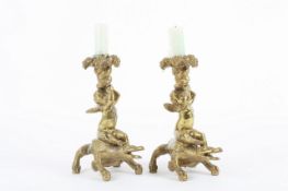 A pair of brass figural candlesticks, depicting cherubs riding upon the backs of crocodiles,