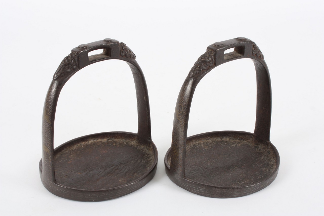 A pair of Chinese cast iron stirrups, with cast animal figure heads to the top, with gilt