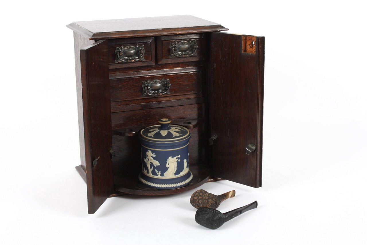 An Arts and Craft oak smokers cabinet, with hinged doors to the front opening to reveal two small