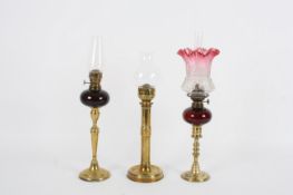 Two Victorian `peg` oil lamps and another, one with etched fluted pink shade and dark red coloured