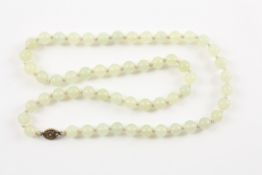 A Chinese pale green jade bead necklace of 57 10mm beads, set with an oval silver filigree clasp.