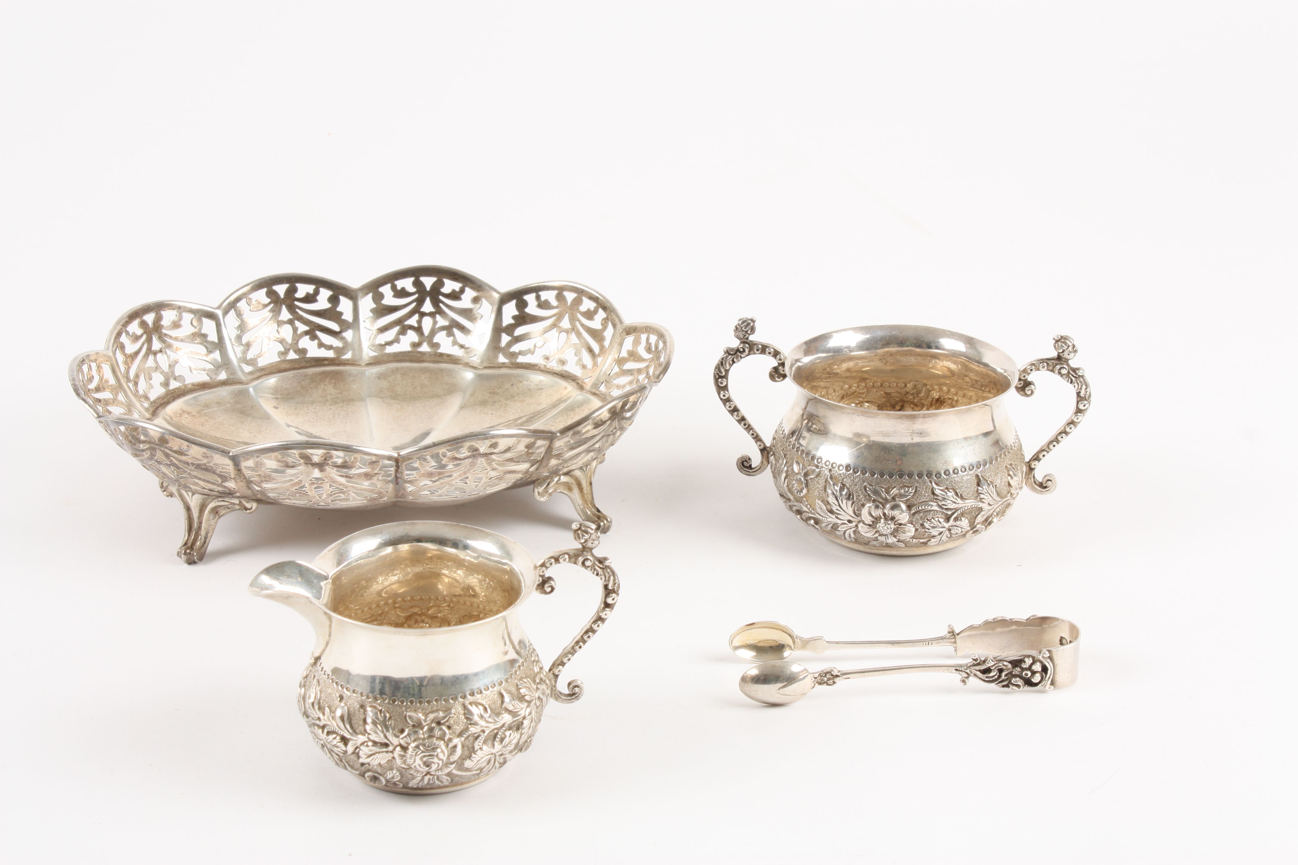 A Victorian embossed silver milk jug, sugar bowls and tongs hallmarked London 1896, the bodies