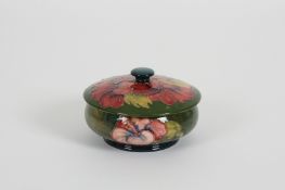 A Moorcroft Iris pattern powder bowl and cover decorated with red flowers on a green ground, with