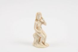 An early 20th century Japanese carved ivory nude figure of a woman seated on a rocky base and