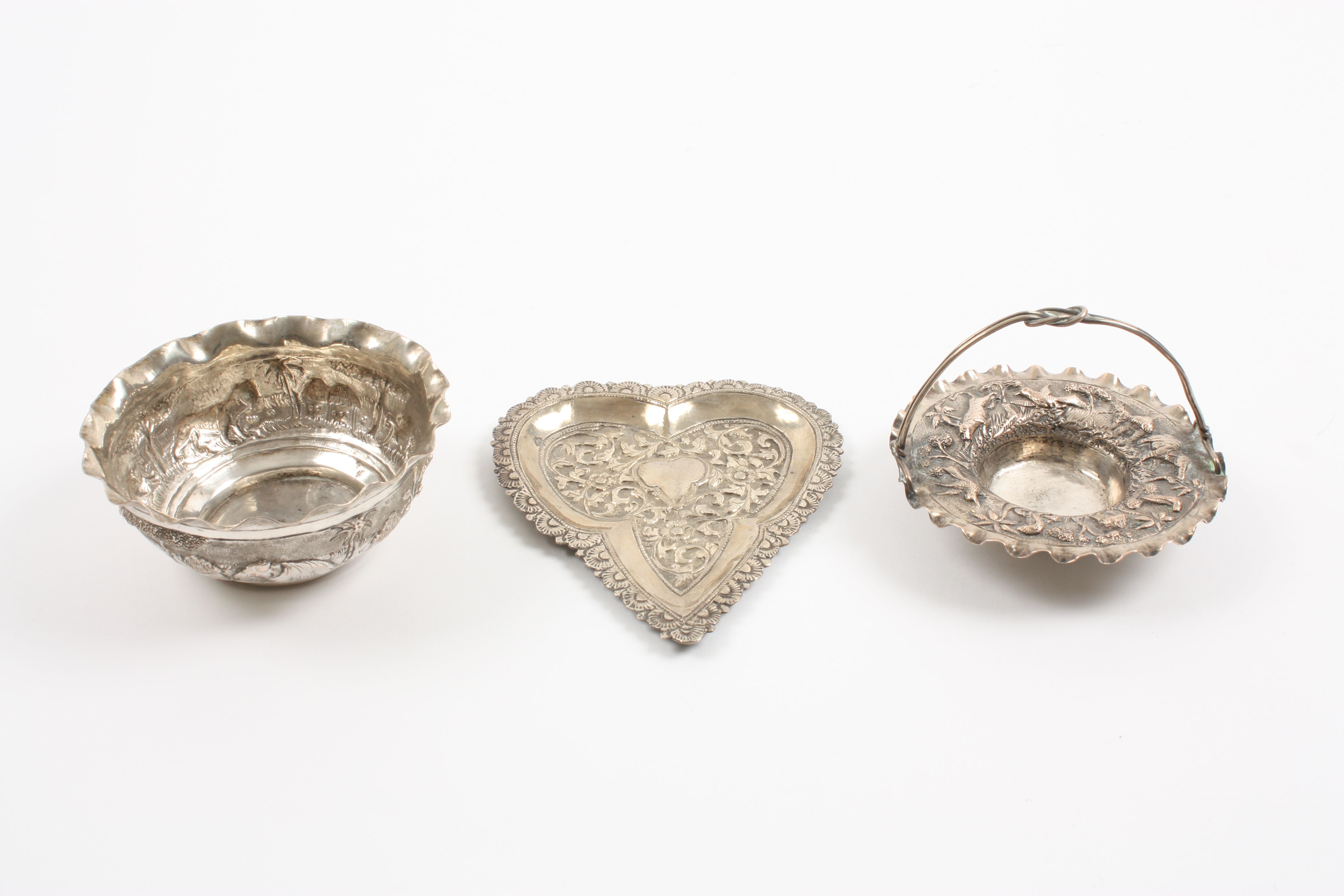 A group of three Indian white metal embossed dishes comprising a heart shaped dish decorated with