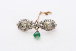 An Edwardian diamond and emerald brooch set with two large pear shaped diamonds in ornate scrolled