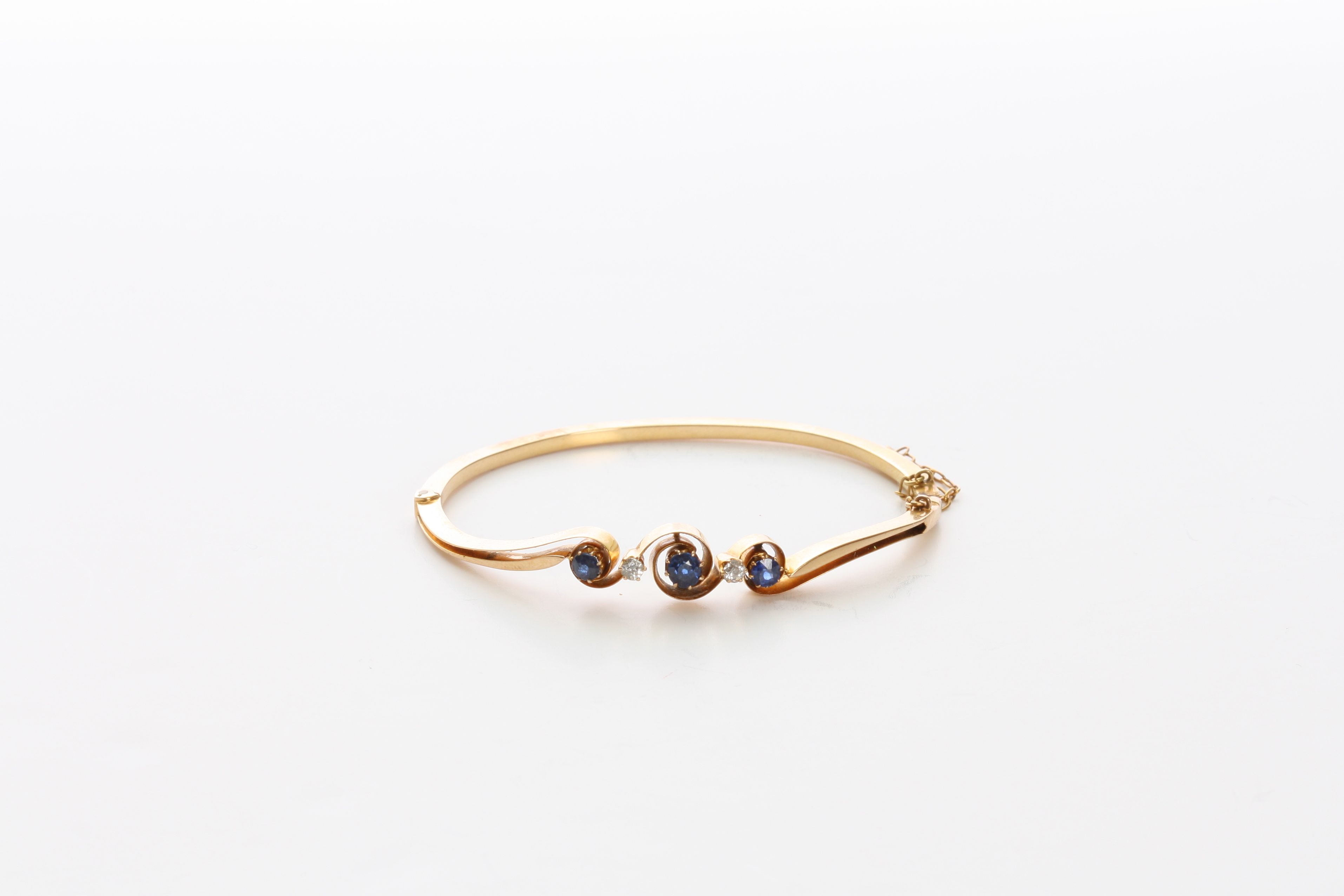 A 9ct gold, sapphire and diamond bangle set with three sapphires of 0.21cts and 0.14cts (2) and
