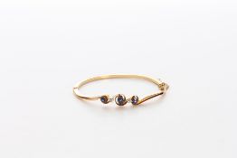 A 9ct gold, sapphire and diamond bangle set with three sapphires of 0.21cts and 0.14cts (2) and