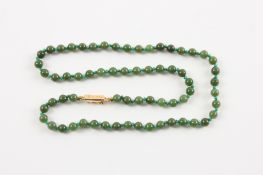 A Chinese dark green fine jade bead necklace of 65 5mm beads, set with a 9ct yellow gold box