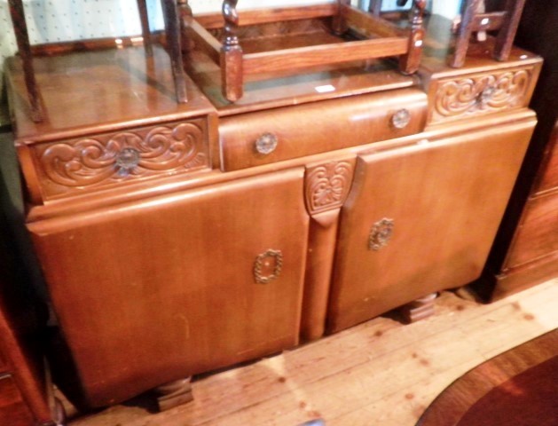 A 1930`s oak sideboard, having a drop centre top over three inline drawers above a pair of cupboard