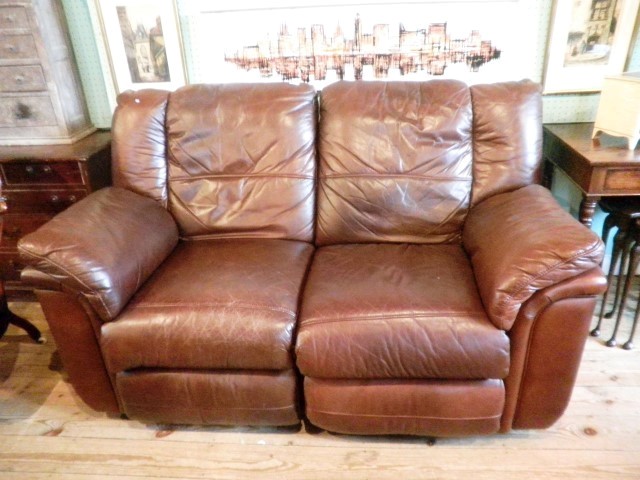 A brown leather two seat reclining settee with integral foot rests.