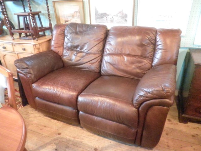 A brown leather two seat reclining settee with integral foot rests.