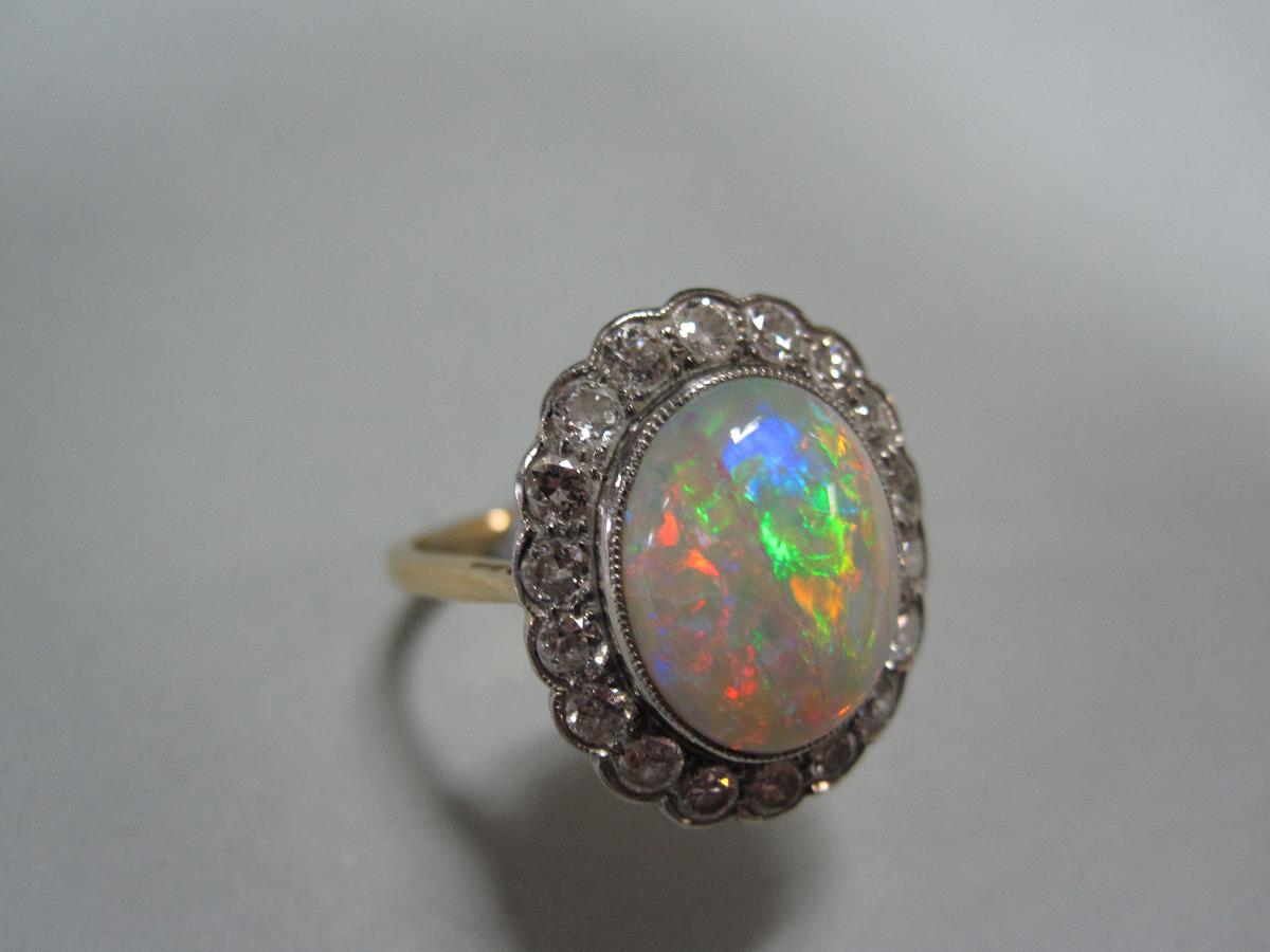 An opal and diamond cluster ring, the oval cabochon opal, exhibiting a fine and rainbow ranged play