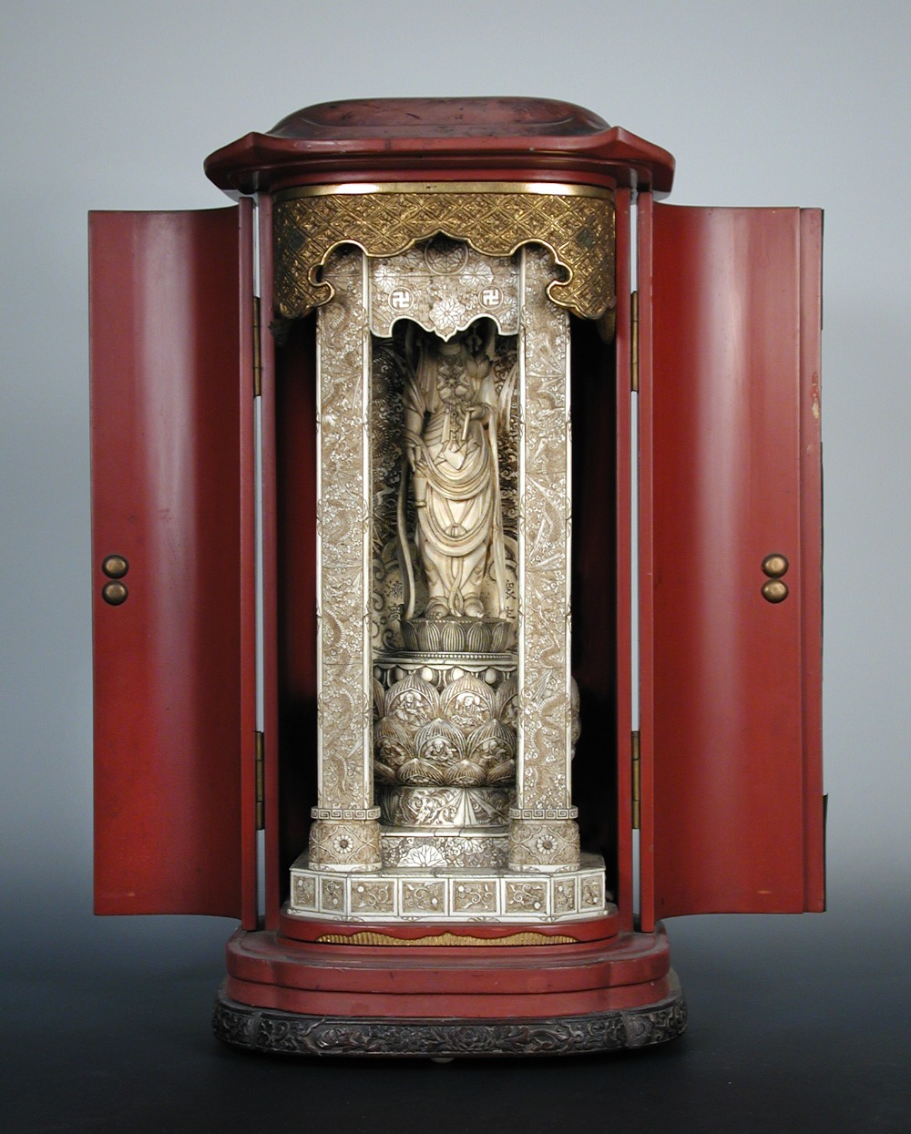 A 19th century red lacquer shrine to Kwannon, the engraved metal mounted doors opening to reveal