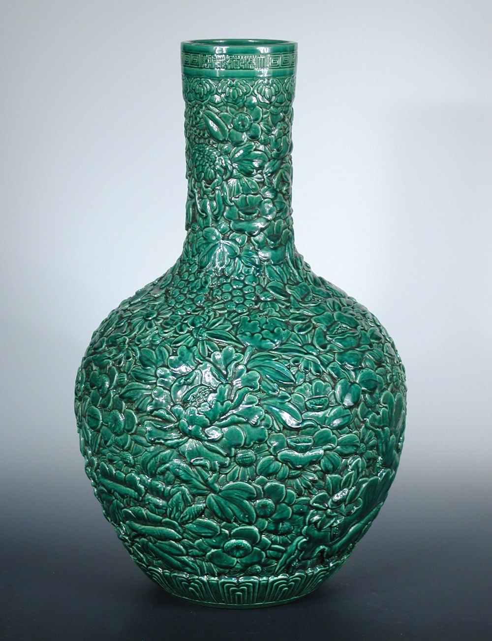 A 20th century decorative green bottle vase, the exterior moulded with flowers, 61cm (24 in) high