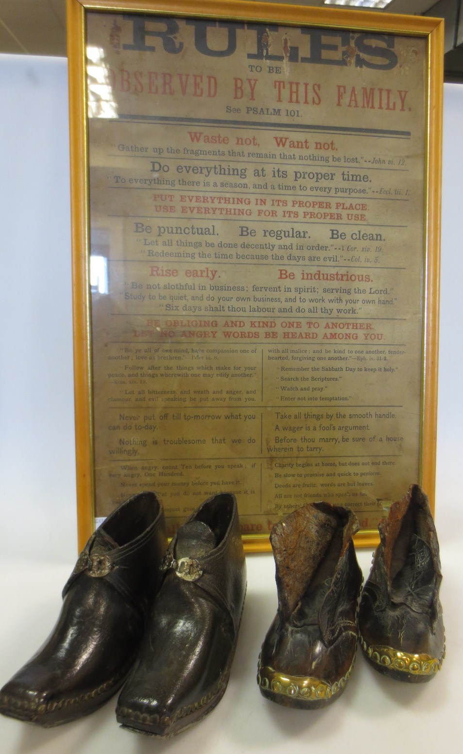 Two pairs of children`s clogs together with a framed print `Rules Observed by the Family`