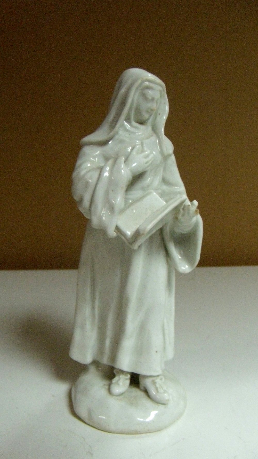 A Bow white glazed figure of a Nun standing on a mounded circular base reading a holy book, 16.
